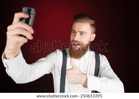 Stylish cheerful young man with beard making photo of himself and showing thumb up