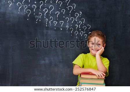 Cheerful encoureged primary school age boy have a lot of question after reading a pile of books
