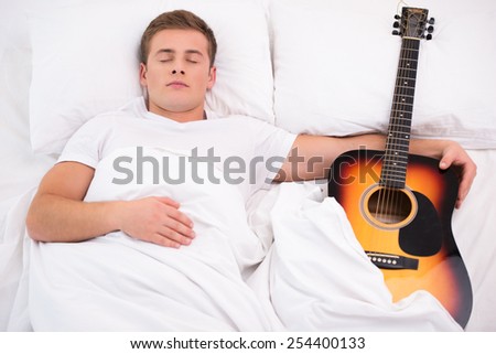 Top view photo of handsome young man sleeping and holding guitar