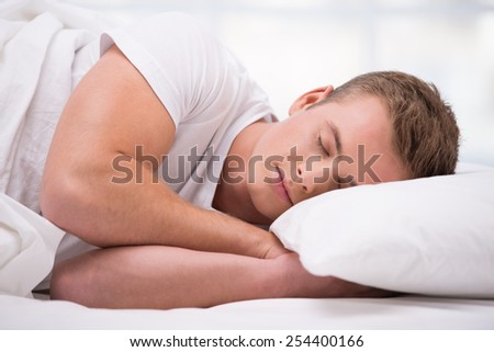 Close up photo of handsome young man. He sleeping comfortably curled under a white blanket