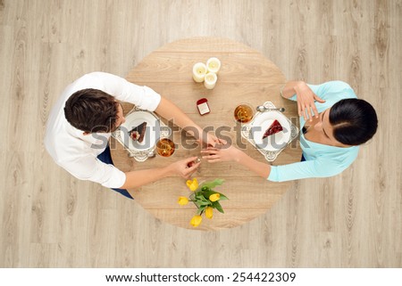 Top view of round table with couple on date. Man putting ring on the left hand of woman. Proposal of marriage concept