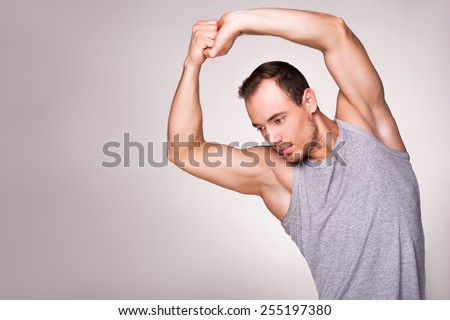 Young handsome well formed man practising sports program, standing on grey background