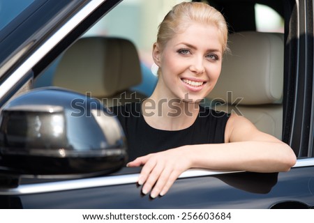 Young smiling woman sitting inside new car and looking at camera. Concept for car rental
