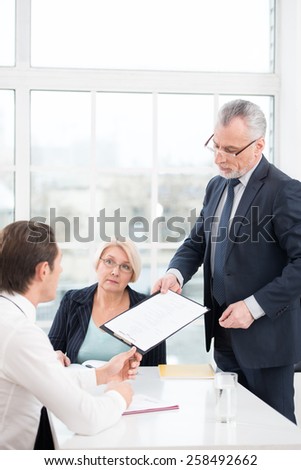 Young man having an interview or business meeting with employers. Director giving prospective employee to complete a questionnaire. Office interior with big window