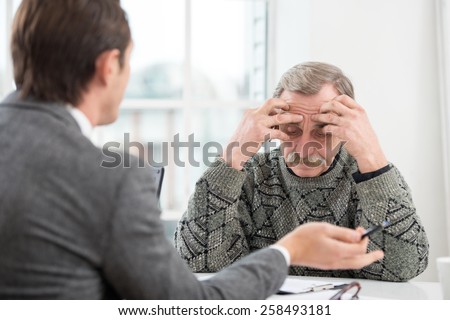 Young businessman having an interview or business meeting with sad old man. Office interior with big window