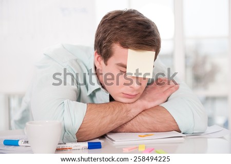 Young tired businessman with sticker on his forehead sleeping while working day. Office interior with window