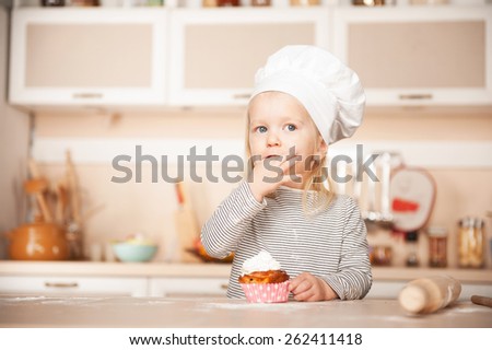 Little cute girl with chef hat tasting cake. Kitchen interior. Concept for young kitchen hands