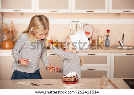 Little cute girl feeding her older sister cake. Kitchen interior. Concept for young kitchen hands