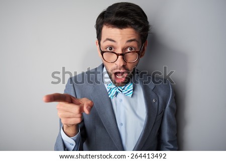 Funny picture of casual young man with glasses wearing jacket and bow tie. Man surprising and pointing at camera