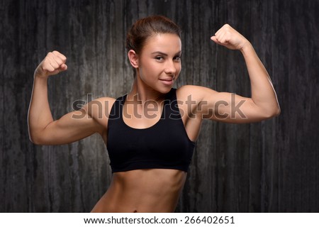 Young mixed race sporty woman wearing black tracksuit for training. She looking at camera and demonstrating her biceps. Fitness concept