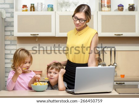 Young business woman early in the morning with her little children. She using laptop. Kitchen interior. Concept for busy mother