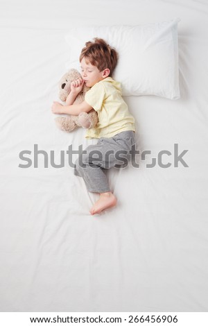 Top view photo of little cute boy sleeping on white bed with teddy bear. Quiet Foetus pose. Concept of sleeping poses
