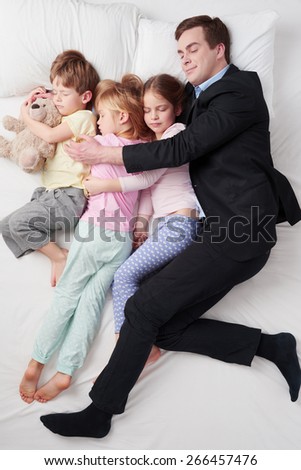 Top view photo of tired businessman wearing suit, and his three children. Father hugging his daughters and son. Children sleeping with father
