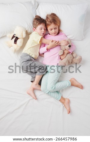 Top view photo of little brother and sister. Children hugging each other. They both sleeping on white bed