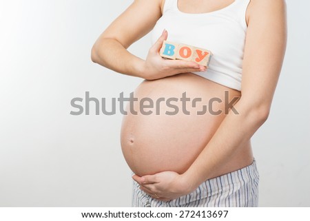 Close up photo of young pregnant woman belly. Woman holding wooden cubes with word \