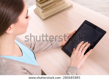 Top view photo of girl working with tablet computer and sitting near stack of books. Concept for teenagers