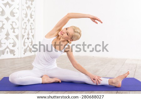 Nice photo of beautiful sporty woman. Woman doing exercises on violet fitness mat and smiling. White interior