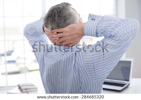 Back photo of businessman in years trying to relax after working. Man throwing his hands behind head