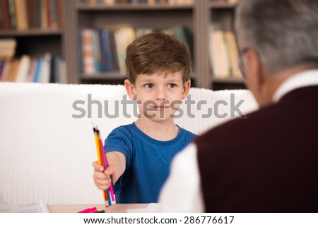 Little boy talking with psychologist. Focus on boy. Boy giving crayons to psychologist. There are many books in psychologist office