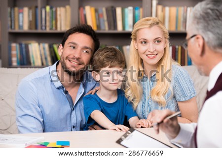 Young family of three talking with psychologist. Psychologist taking notes. There are many books in psychologist office