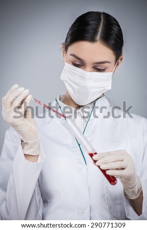 Woman wearing protective clothing, medical mask and gloves. Woman holding test tube and filling it