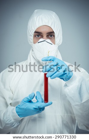 Man wearing protective clothing, dust mask and gloves. Man holding test tube and looking at camera