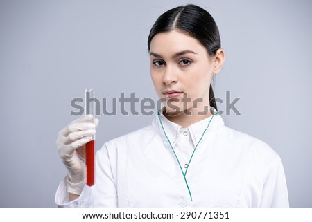 Woman wearing protective clothing and gloves. Woman holding test tube and looking at camera