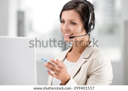 Beautiful smiling woman with headphones using laptop while searching information at call center