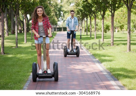 Portrait of beautiful young woman and handsome man. Girl and boy using segway. Girl smiling. Green alley as background