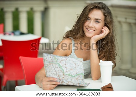 Portrait of beautiful young woman on vacation. Girl studying map, cheerfully smiling, drinking coffee and looking at camera