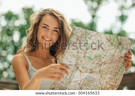 Portrait of beautiful young woman on vacation. Girl studying map, cheerfully smiling and looking at camera