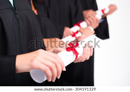 Close up photo of young students dressed in black graduation gowns. Isolated on white background. Students holding diplomas