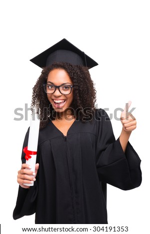 Young Afro American girl student dressed in black graduation gown. Isolated on white background. Girl cheerfully smiling, holding diploma and showing thumb up