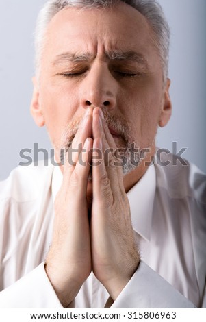 Portrait of concentrated old man praying to God with closed eyes