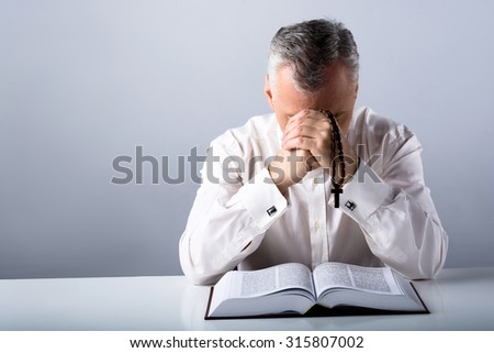 Photo of sad old man praying to God with rosary and open Bible