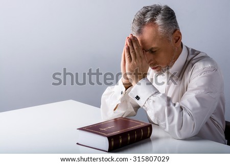 Photo of concentrated old man praying to God with Bible on table