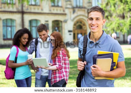 Photo of young group of students with backpacks and books. Campus as a background. Boy with notebooks looking at camera. Students are on background
