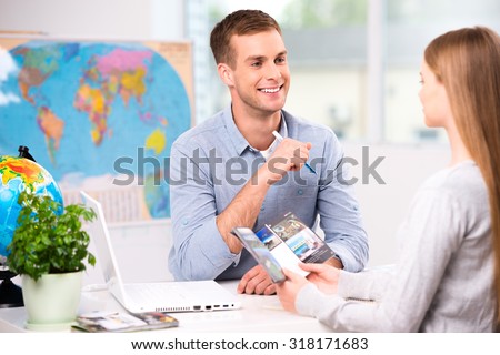 Photo of male travel agent and young woman. Young man smiling and offering vacation options for female tourist. Travel agency office interior with big world map