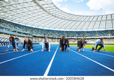 Photo of confident multi ethnic business people lined up getting ready for race on modern sport track. Stadium as a background