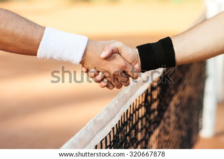Close up photo of young men on tennis court. Men playing tennis. Men shaking hands above net before game