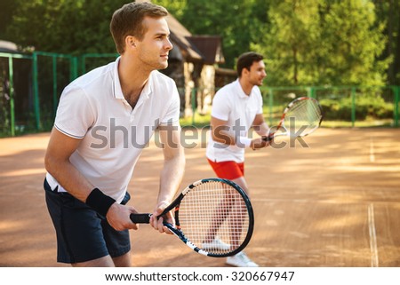 Picture of handsome young men on tennis court. Men playing tennis. Man is ready to hit tennis ball. Beautiful forest area as background