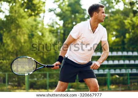 Picture of handsome young man on tennis court. Man playing tennis. Man hitting tennis ball. Beautiful forest area as background