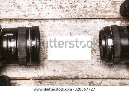 Top view close up photo of two professional cameras and blank visit card. Objects are on light colored wooden floor