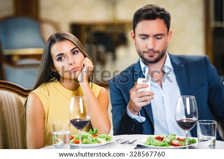 Photo of romantic dinner in expensive hotel. Young woman is bored and lonely while her boyfriend using mobile phone
