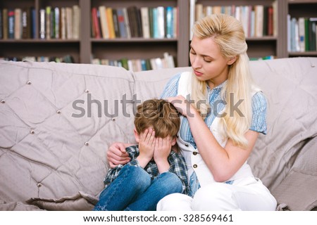 Little boy talking with female psychologist. Boy crying. There are many books in psychologist office