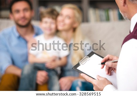 Young happy family of three talking with psychologist. Focus on psychologist. There are many books in psychologist office