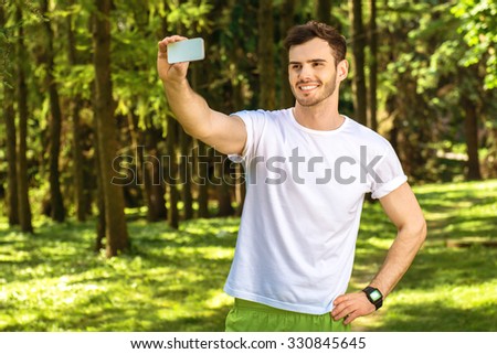 Photo of handsome nice guy outdoors at morning. Young man smiling and making selfie photo on mobile phone while running in park