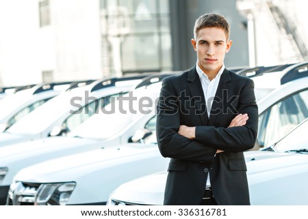 Photo of young male consultant in auto show. Consultant standing near row of cars and looking at camera. Concept for car rental