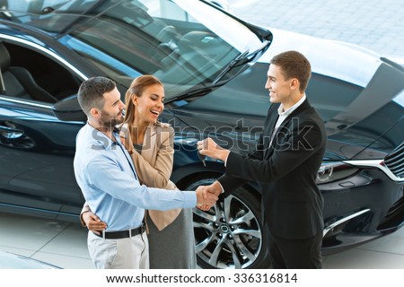 Top view photo of young male consultant giving car key to buyers after successful deal in auto show. Concept for car rental
