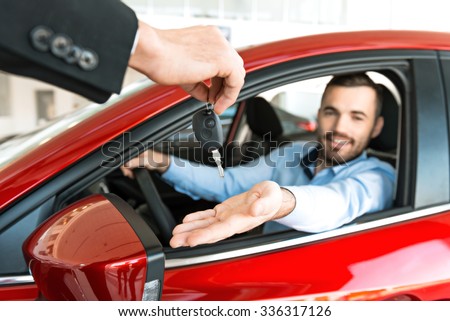 Photo of young man sitting inside new car and getting keys to it. Concept for car rental